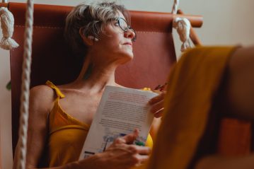 Mulher adulta, com a pele com linhas de expressão, lendo um livro